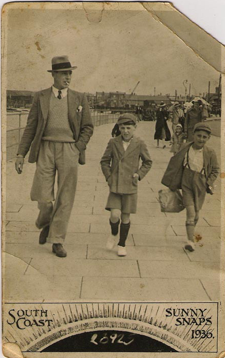 Postcard image of a man with two young boys walking along a seaside promenade in 1936
