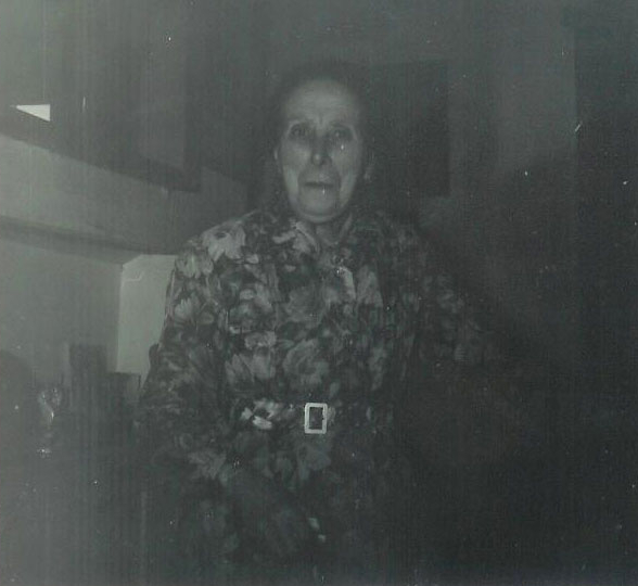 Gloomy black white photograph of a severe-looking elderly lady in a flowery dress