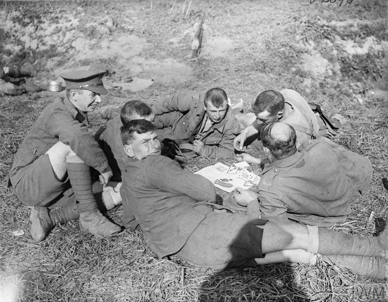 Black and white photo of a group of 6 men in Army uniform playing cards. One man looks back over his shoulder at the camera.