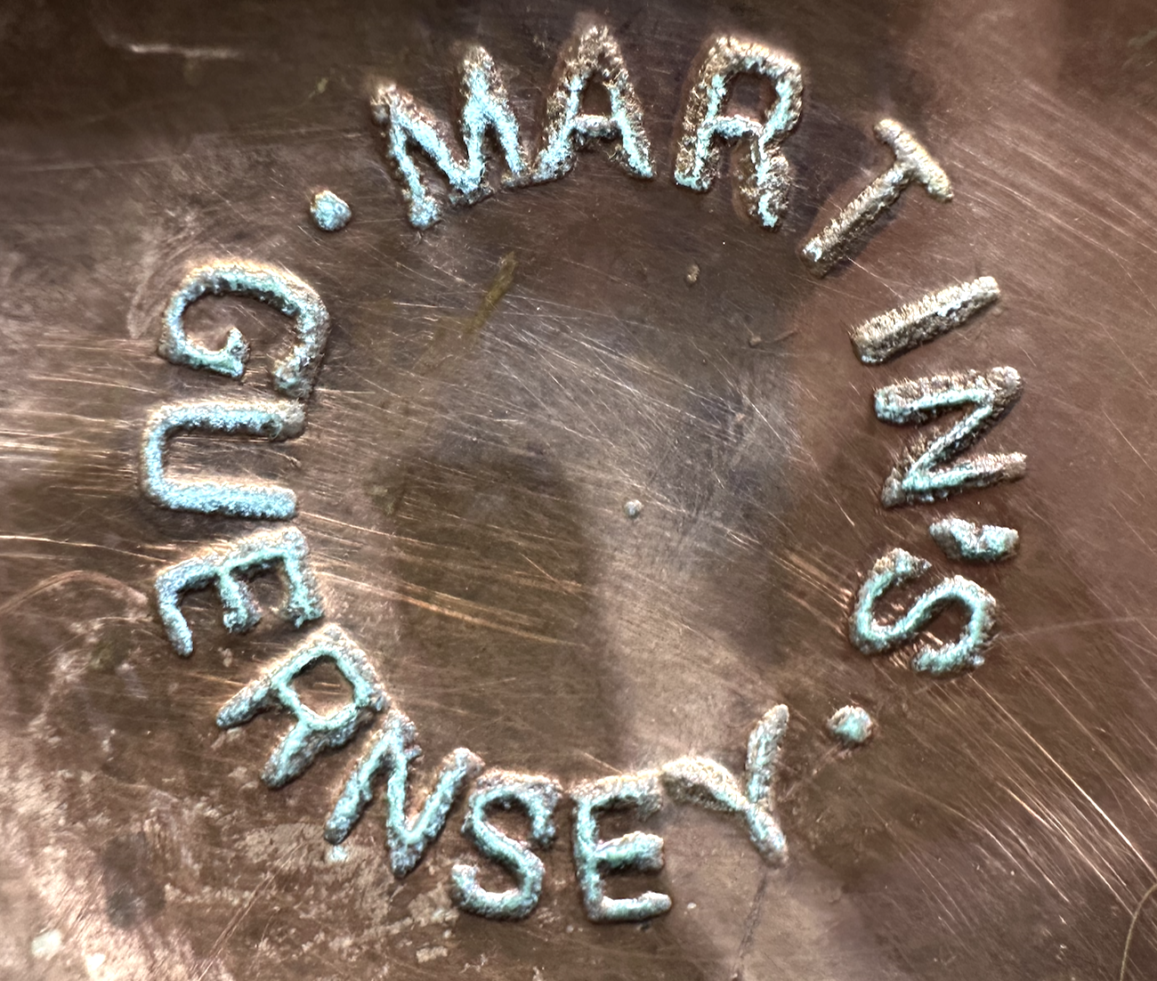 Close up of the base of a copper Guernsey milk can showing the maker's name 'Martin's Guernsey'