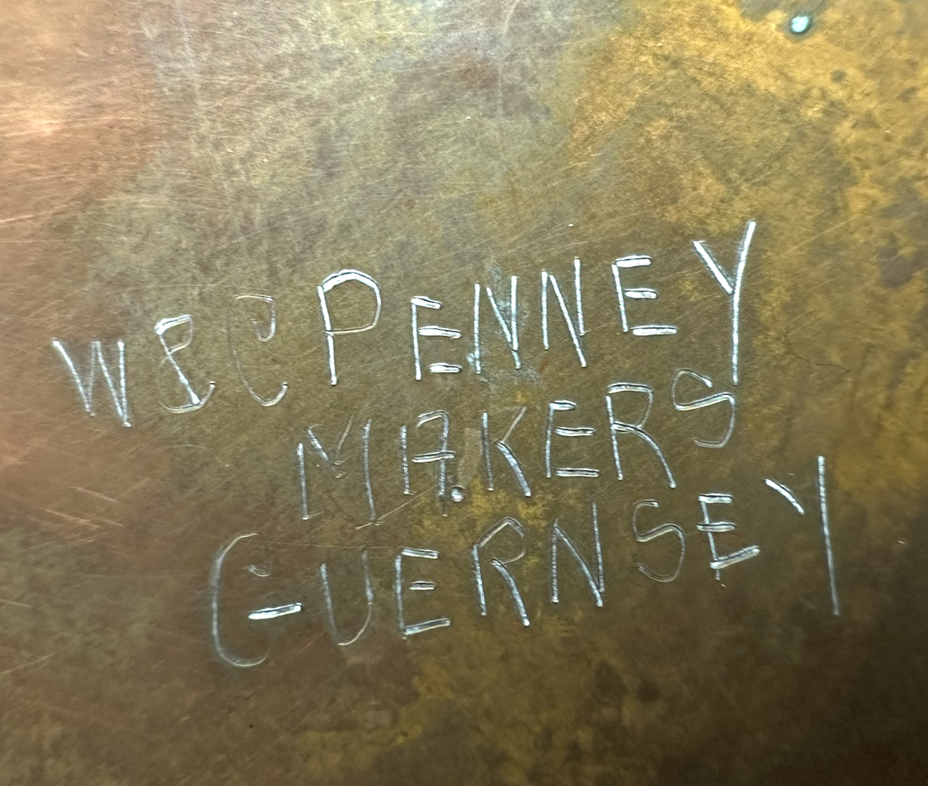 Close up of the base of a copper Guernsey milk can showing the name W&C Penney Makers Guernsey