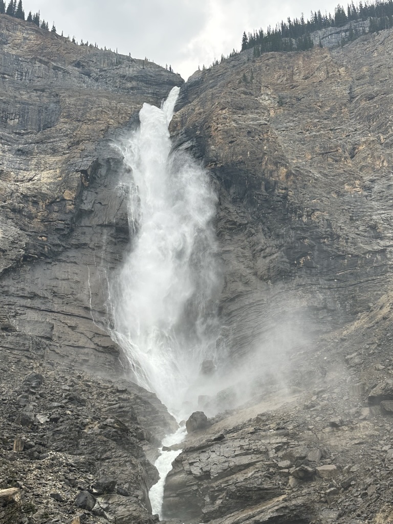 photo of a high waterfall cascading down a sheer rockface with some fir trees at the top of the cliff