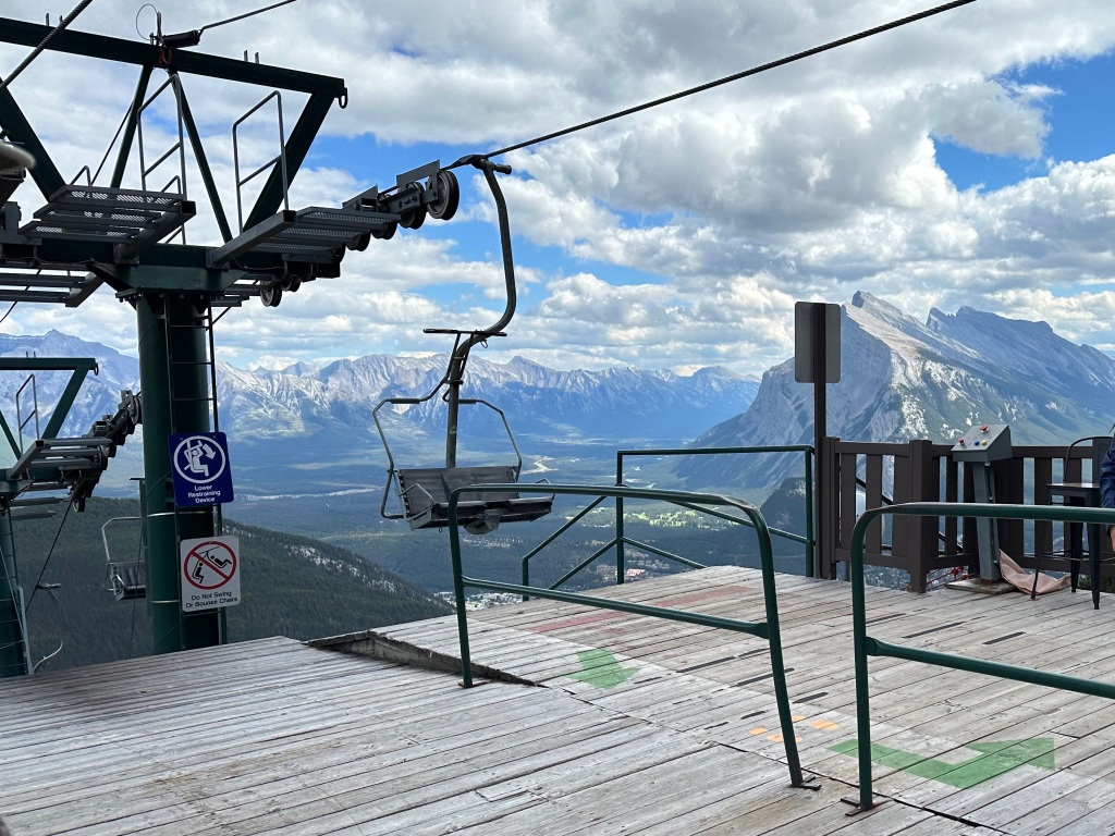 A mountain chairlift with mountain ranges in the middleground and background
