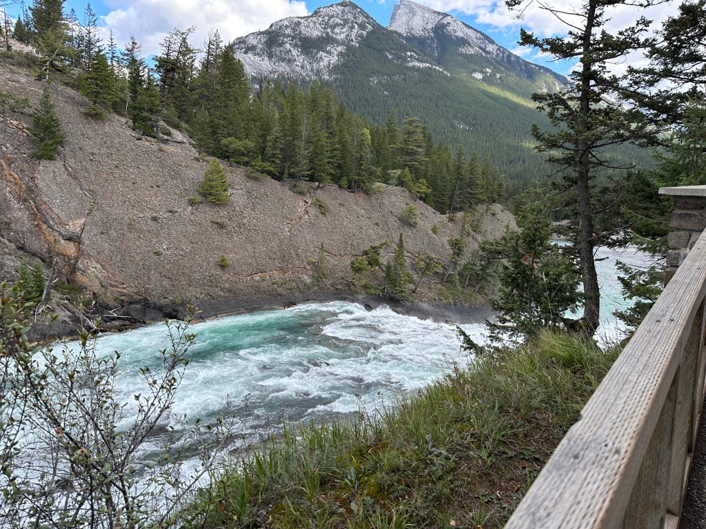 Turbulent waterfall on the Bow River with forest covered mountains in the background