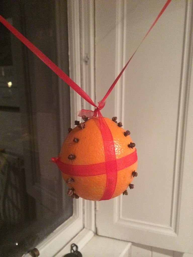 A scented pomander made from an orange stuck with cloves and tied with ribbon and