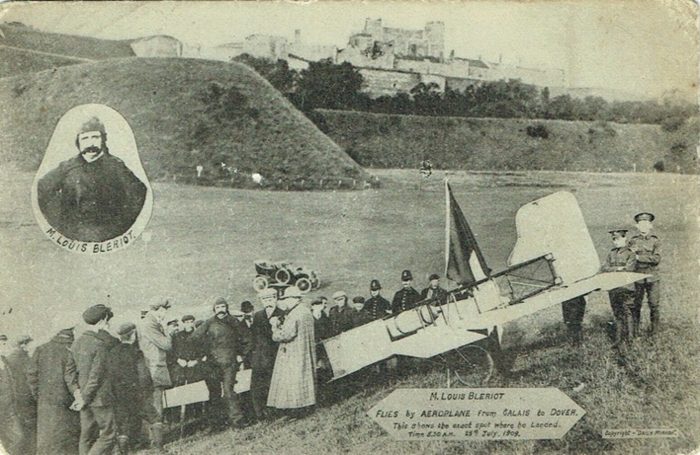 Black and white postcard showing Louis Bleriot's plane having flown from Calais to Dover surrounded by people. There is a horseless carriage in the mid ground and Dover Castle in the background. There is a little cut-out portrait of Louis Bleriot.