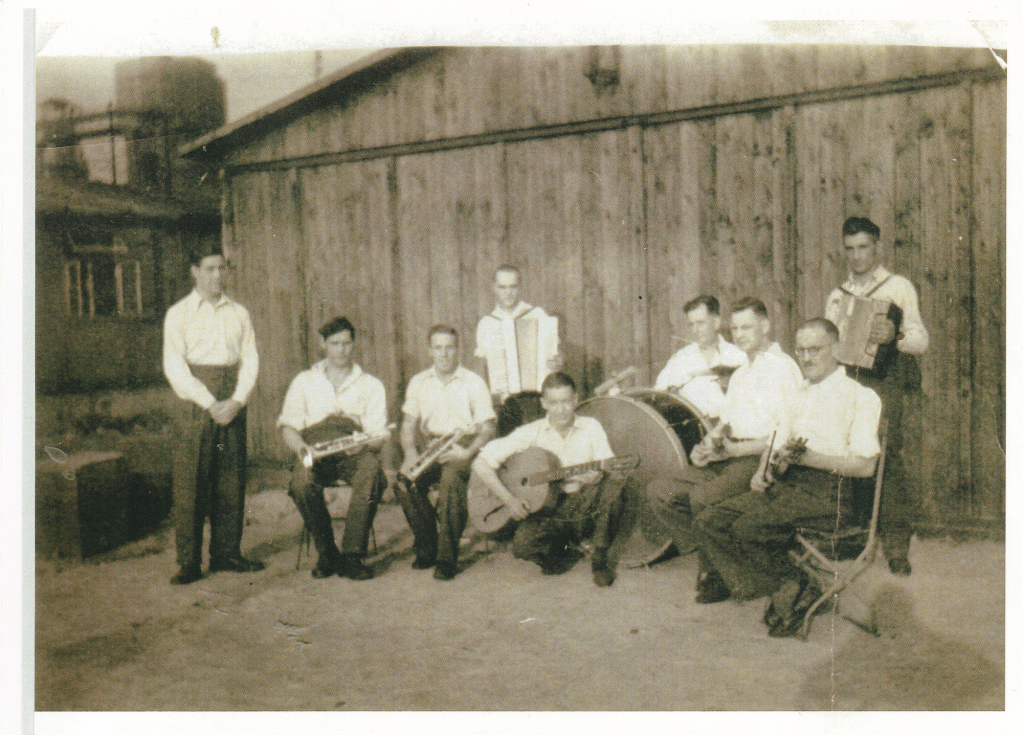 Group photo of 9 WW2 prisoners of war each holding a muscal instrument at E72 workcamp attached to Stalag VIIIB POW camp near Lamsdorf
