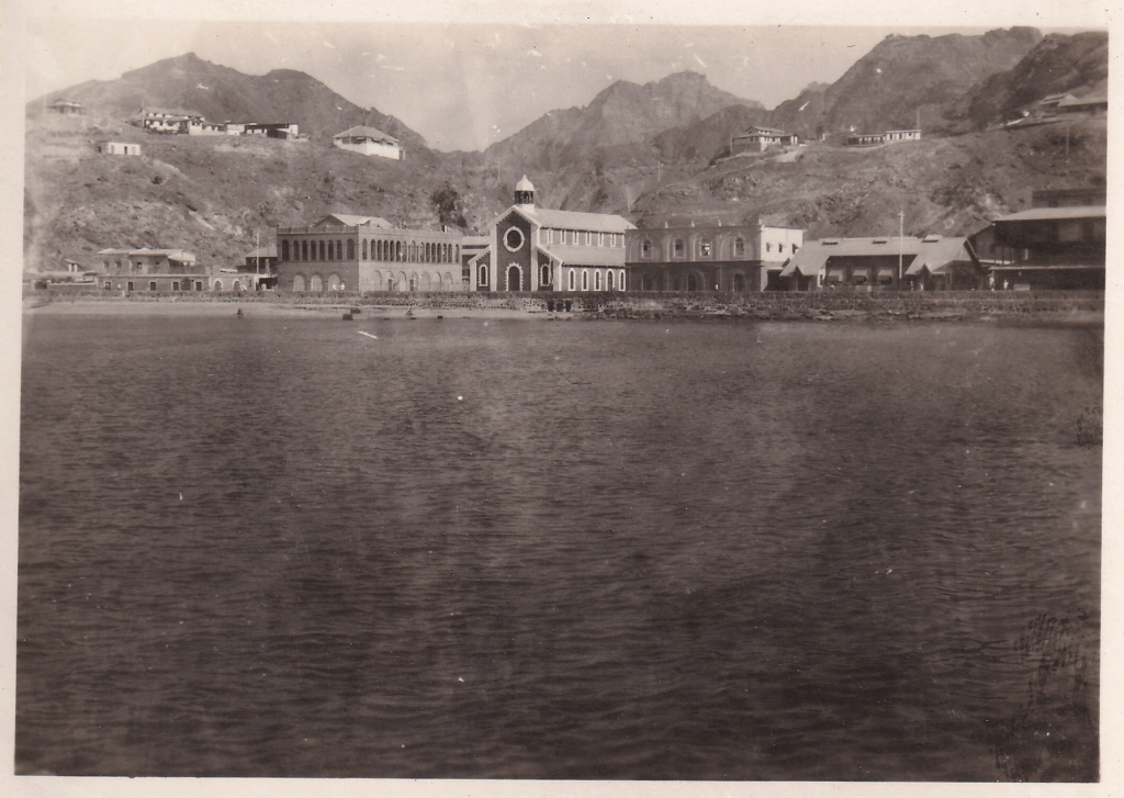 Black and white photograph of Post Office Bay, Steamer Point, Aden with large buildings along the waterfront and mountains behind with some smaller buildings c.1945