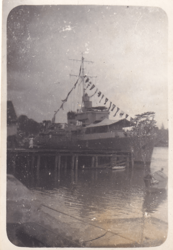 Black and white photograph of HMS Pickle bedecked with flags moored by a pier in Kuching, Sarawak, Borneo c.1945