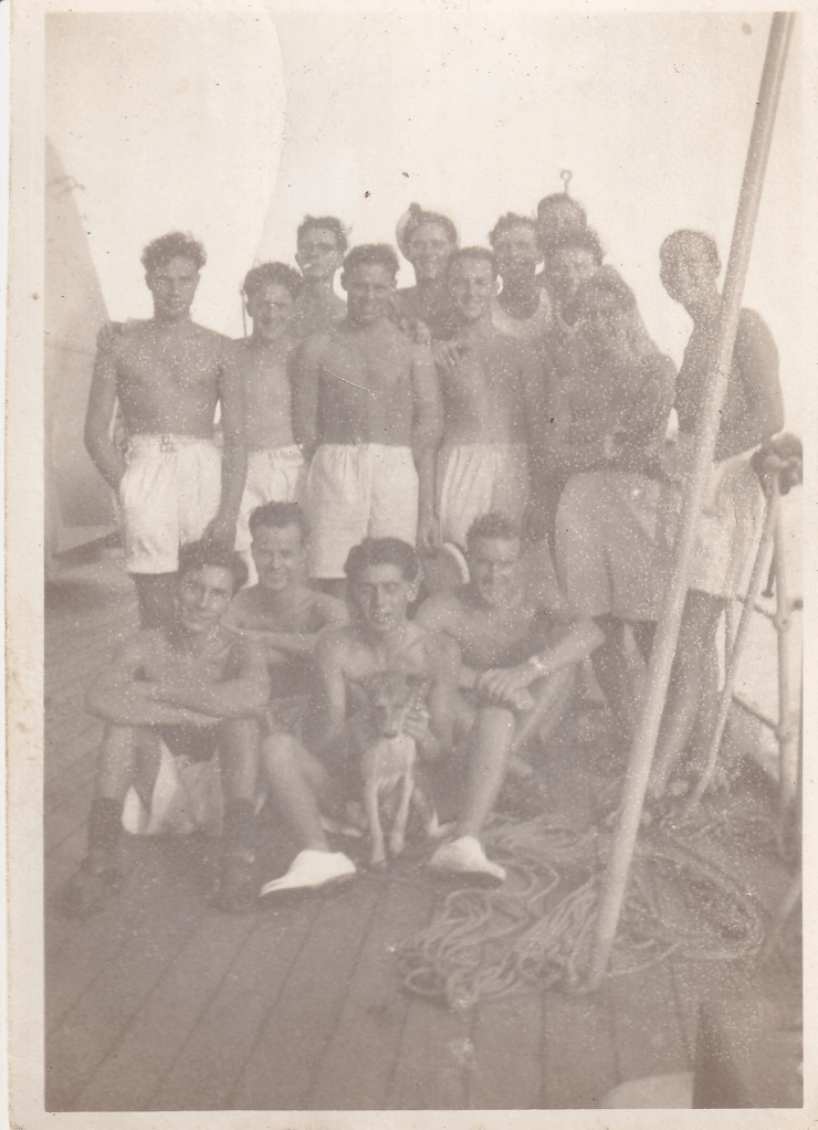 A group of young men some standing, some sitting, all dressed in white shorts, presumed to be part of the crew of HMS Pickle. One is holding a small dog.