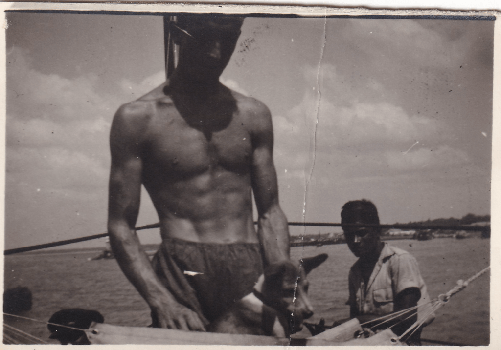 Black and white photograph of a young man with a small dog on a boat.