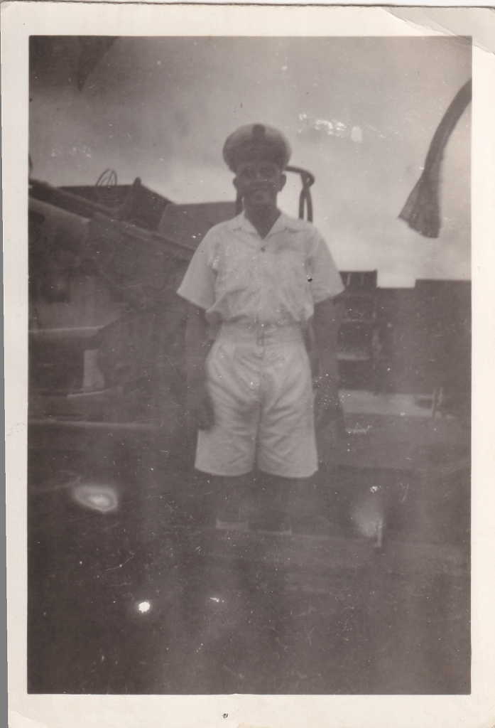 Black and white photograph of a young naval officer in tropical uniform aboard a ship c.1945