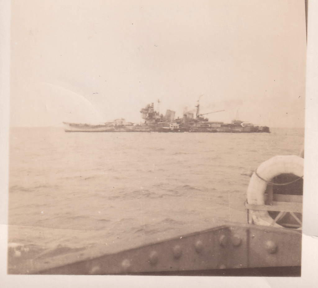 Black and white photograph taken from a ship showing the Japanese cruiser Myōkō with heavily damaged stern moored in Singapore Harbour c. 1945