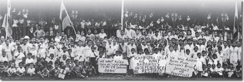 Black and white image of a large group of people of all ages with many children in the front row.  Some of the crowd carry flags and others hold anti-cessionist placards