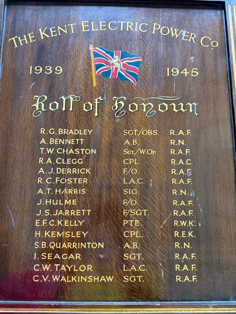 A framed wooden memorial board dedicated to the Kent Electric Power Company, featuring a Union flag and the names, ranks, and services of fifteen men who lost their lives during World War II, inscribed in gold.