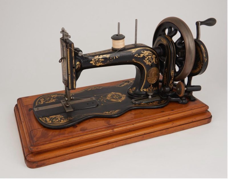 A vintage Singer sewing machine with intricate gold designs on a black body, placed on a wooden base.