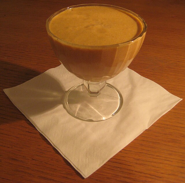 A glass dessert cup filled with a creamy, mousse-like dessert, sitting on a white napkin against a wooden table.