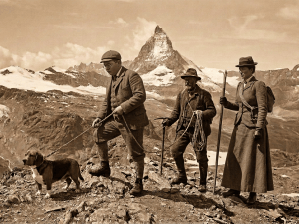 Three mountaineers and a dog crossing rocky terrain beneath the Matterhorn